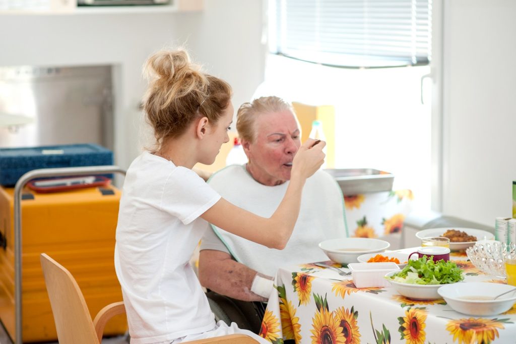 Nurse In The Nursing Home Helping Senior Woman Eating