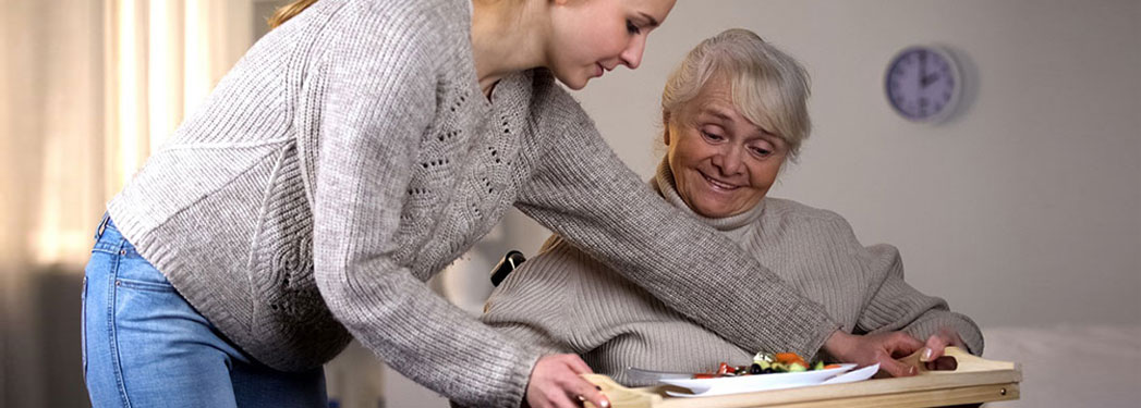 Female volunteer serving dinner to handicapped old woman, elder care, help